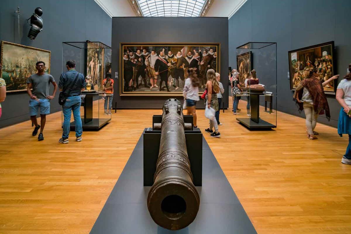 People in a large gallery/hall. a large cannon is in the middle of the room