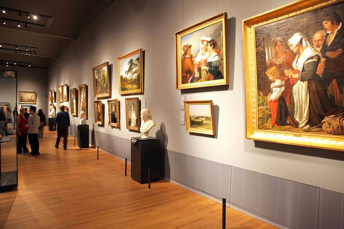 Gallery room with paintings and statues and people viewing