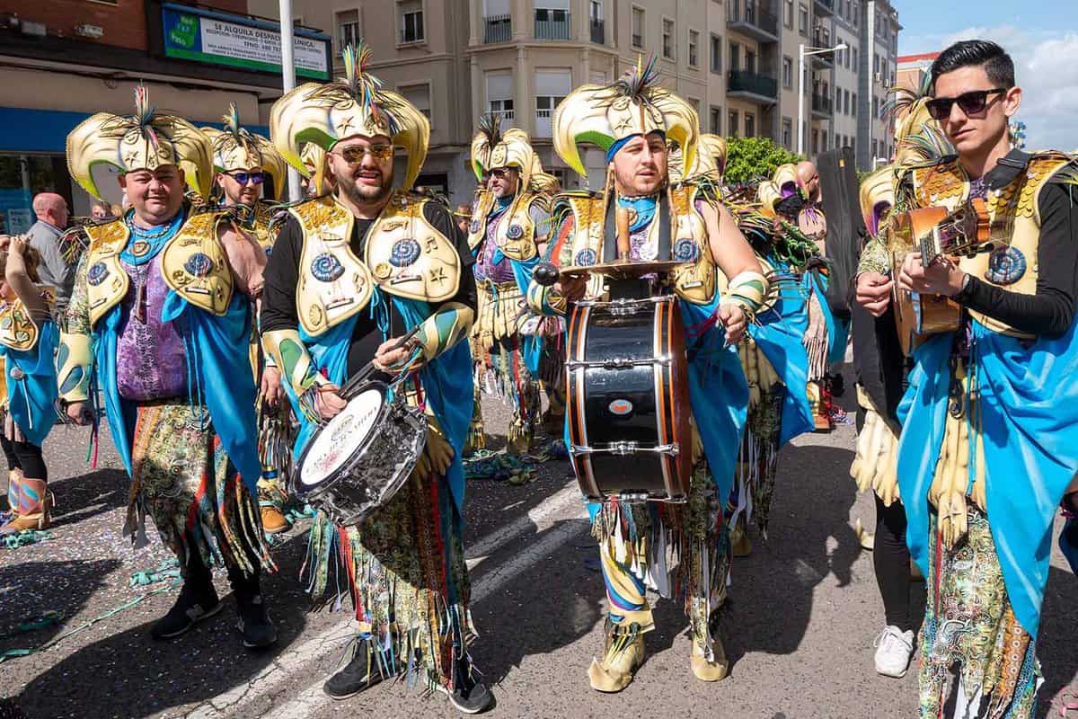 A marching band in matching colourful dress with bright blue trousers and gold headdresses parade in the street