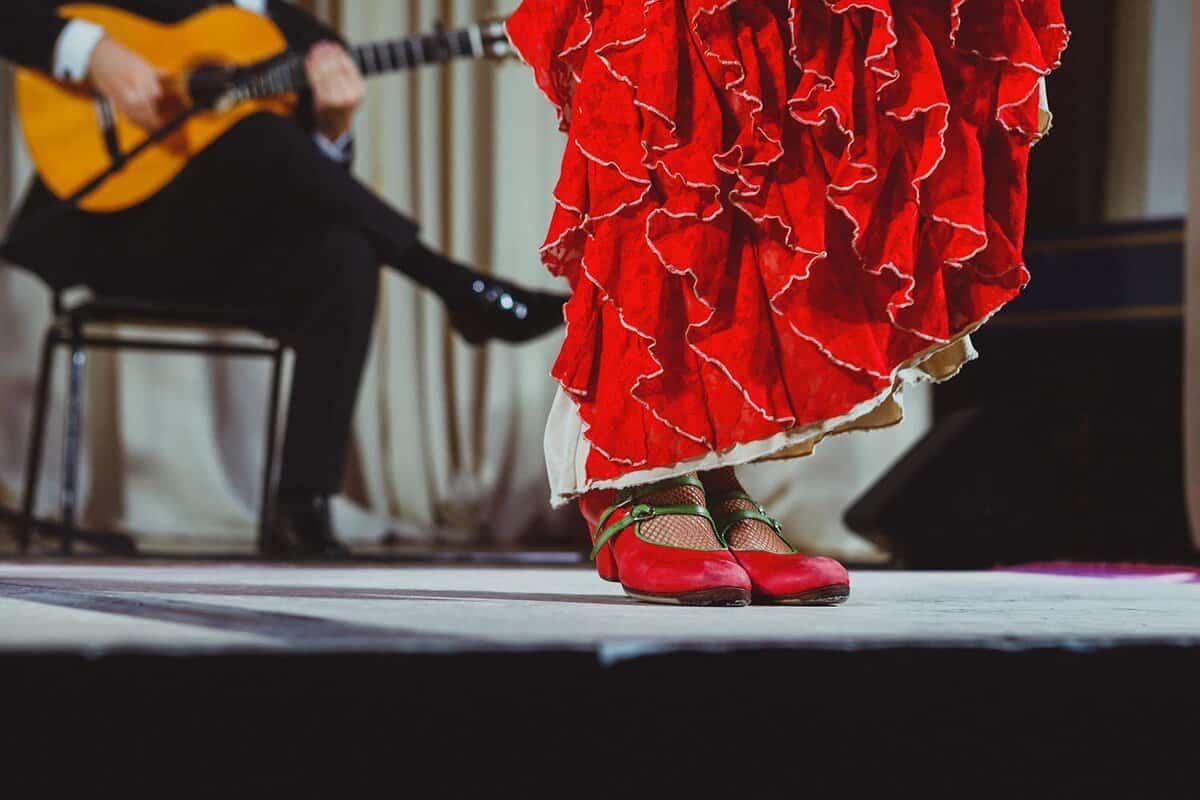 Photo of flamenco dancers feet and bottom of her red dress, on a stage