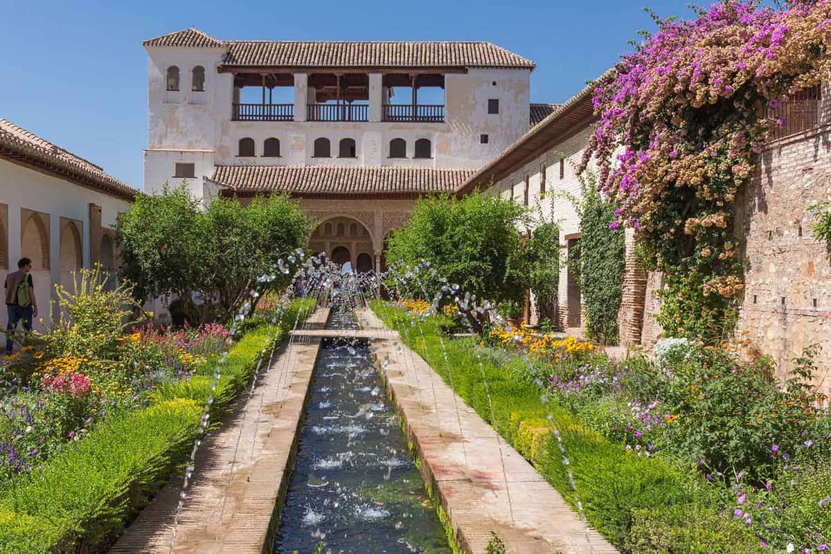 View of the courtyard full of flowers, with a long central pool and small fountain jets pouring into it