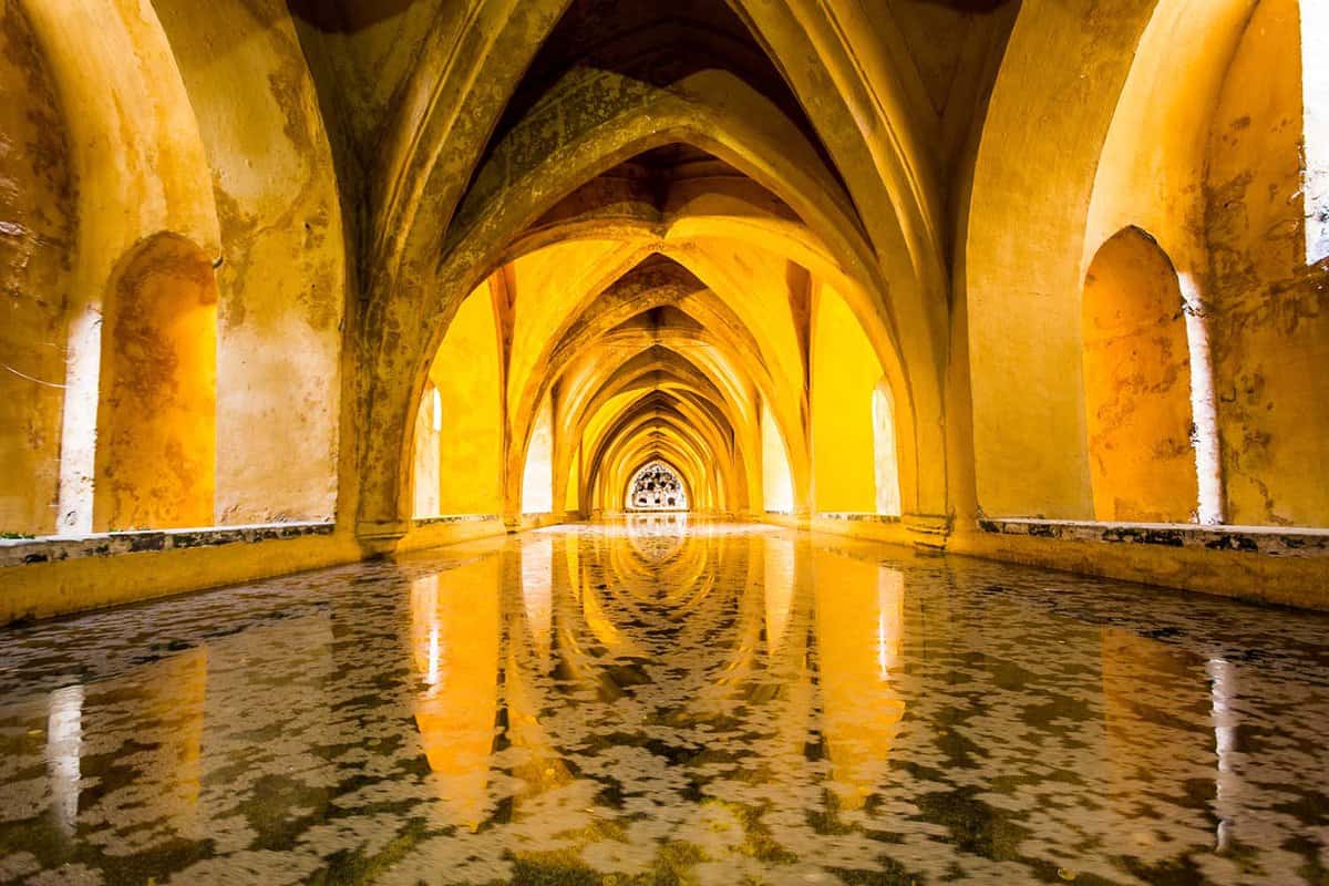 View of a long arabic bath beneath a vaulted ceiling, bathed in golden yellow light