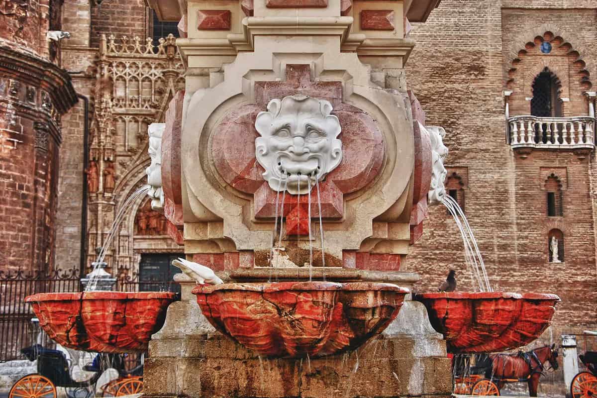 Close up of a fountain within the cathedral courtyard, water pours out of lion faces