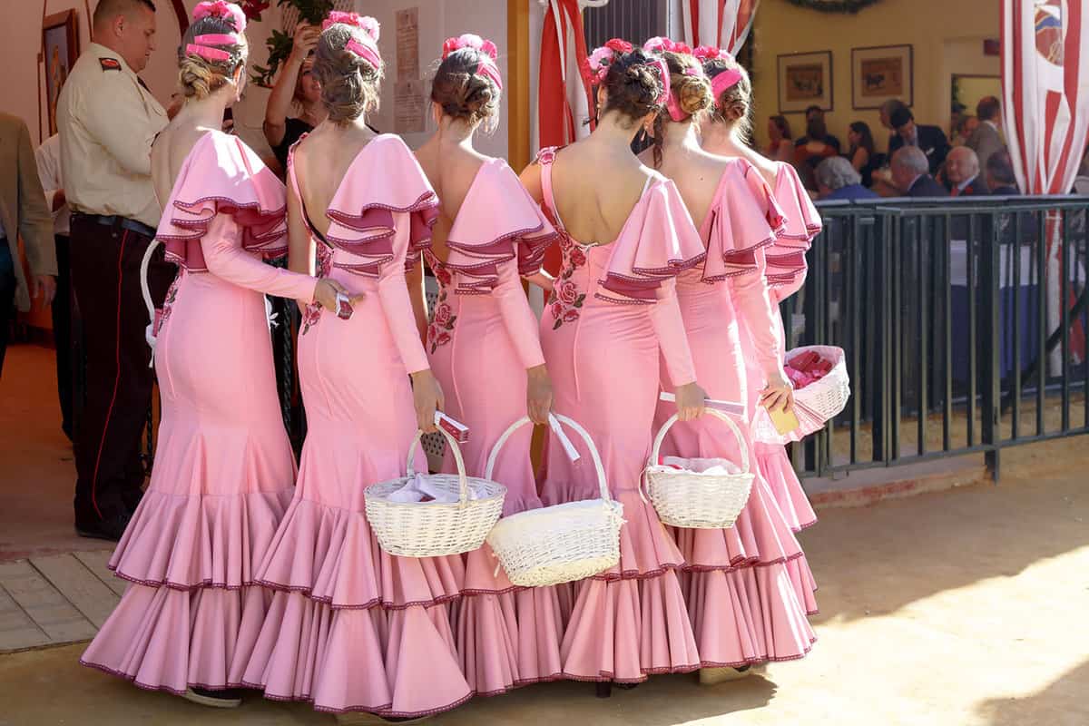 Women lined up wearing matching pale pink flamenco dresses, holding white baskets