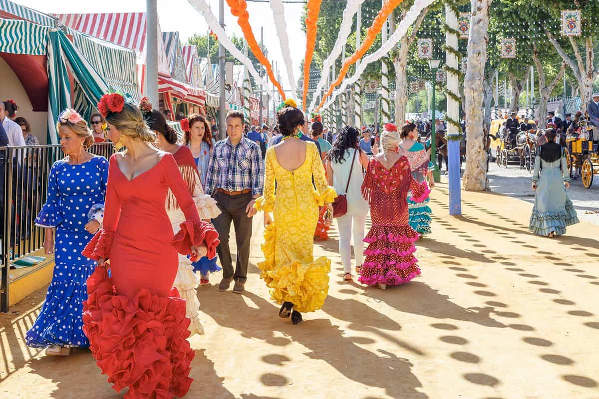Women wearing traditional flamenco dresses walk down the streets of the feria