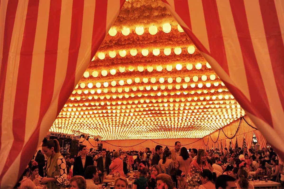 People in indoor tent seating, where the ceiling is illuminated by string lights