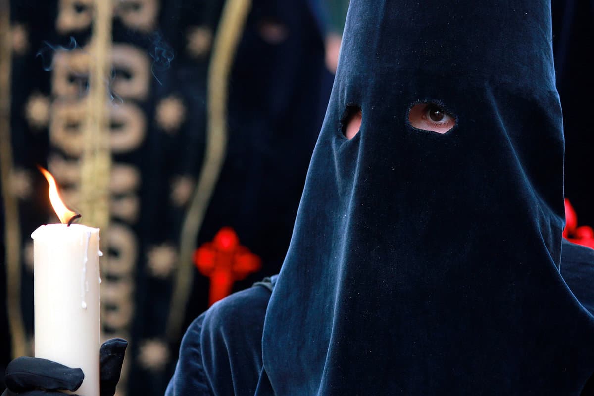 Close up of person wearing black pointed hood holding a candle