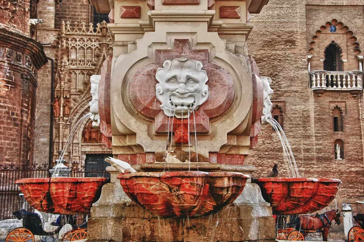 Close up of a beautiful fountain in red and gold stone, with 3 different jets coming from the mouths of lions