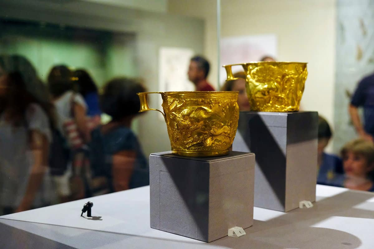 Two gold cups on display, while visitors walk around