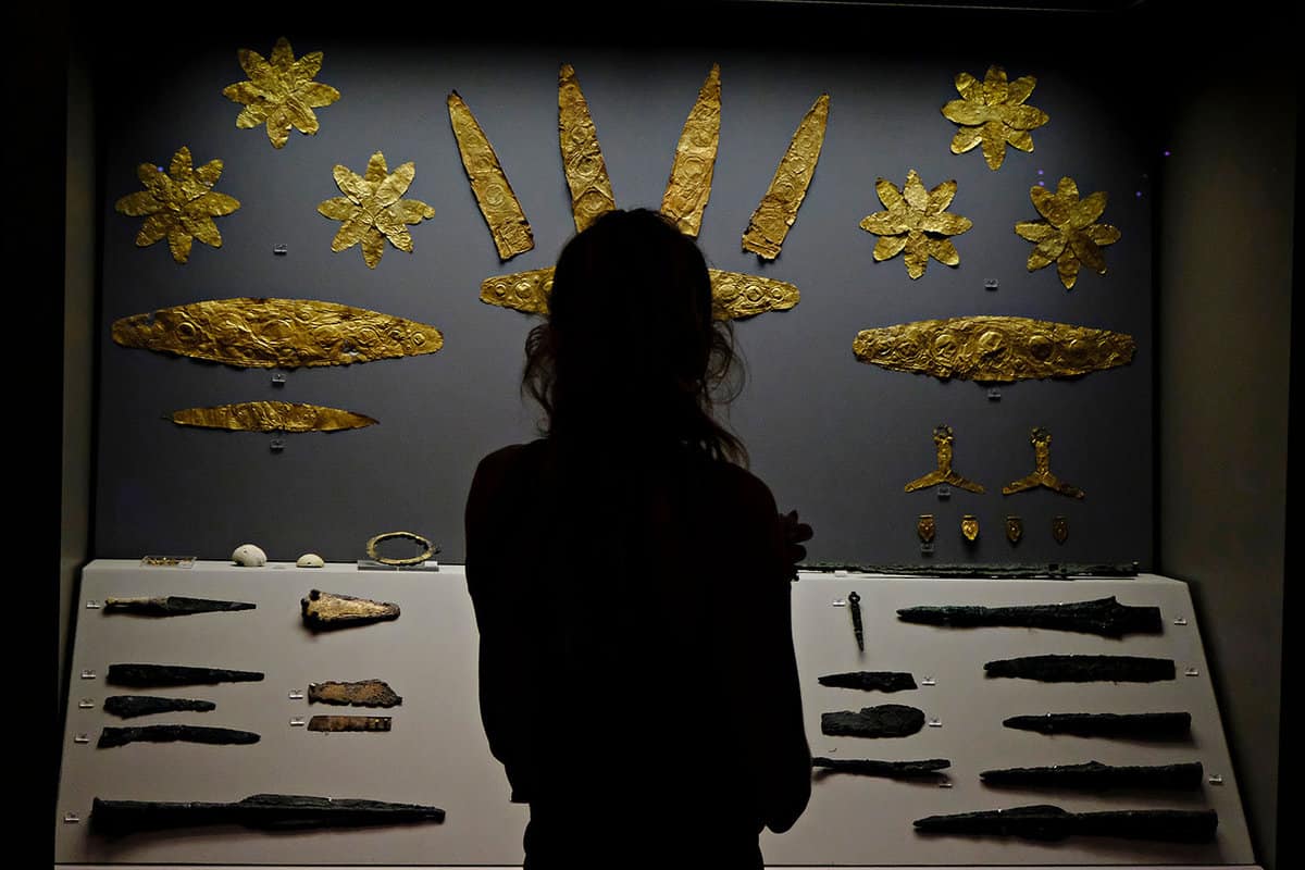 A visitor stands in front of a display of hammered golden items