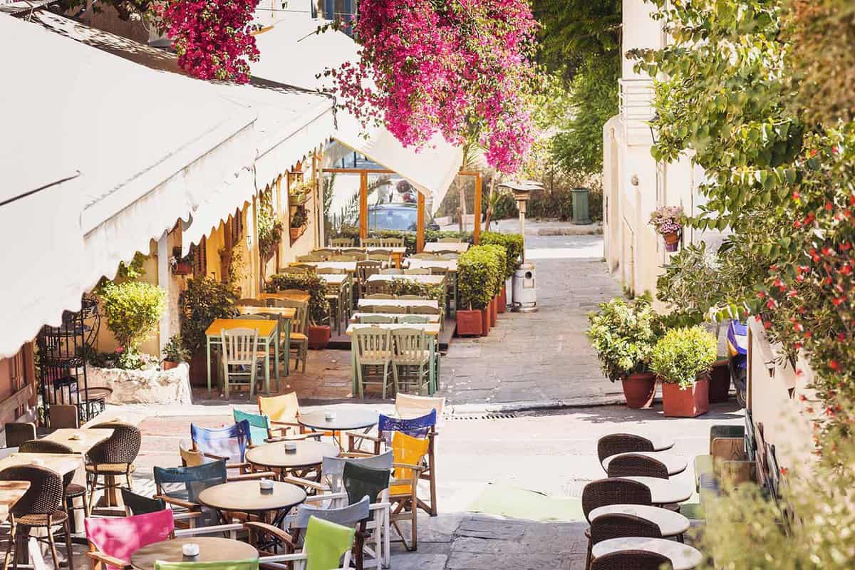 A sunlit street with empty outdoor seating in Plaka