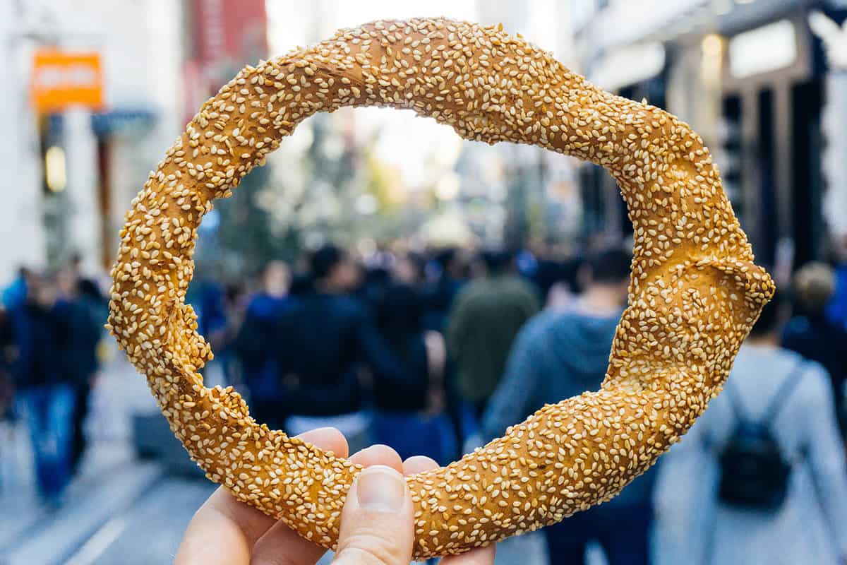 A Greek sesame bread ring koulouri (greek bagel) held in front of Athens' main shopping street