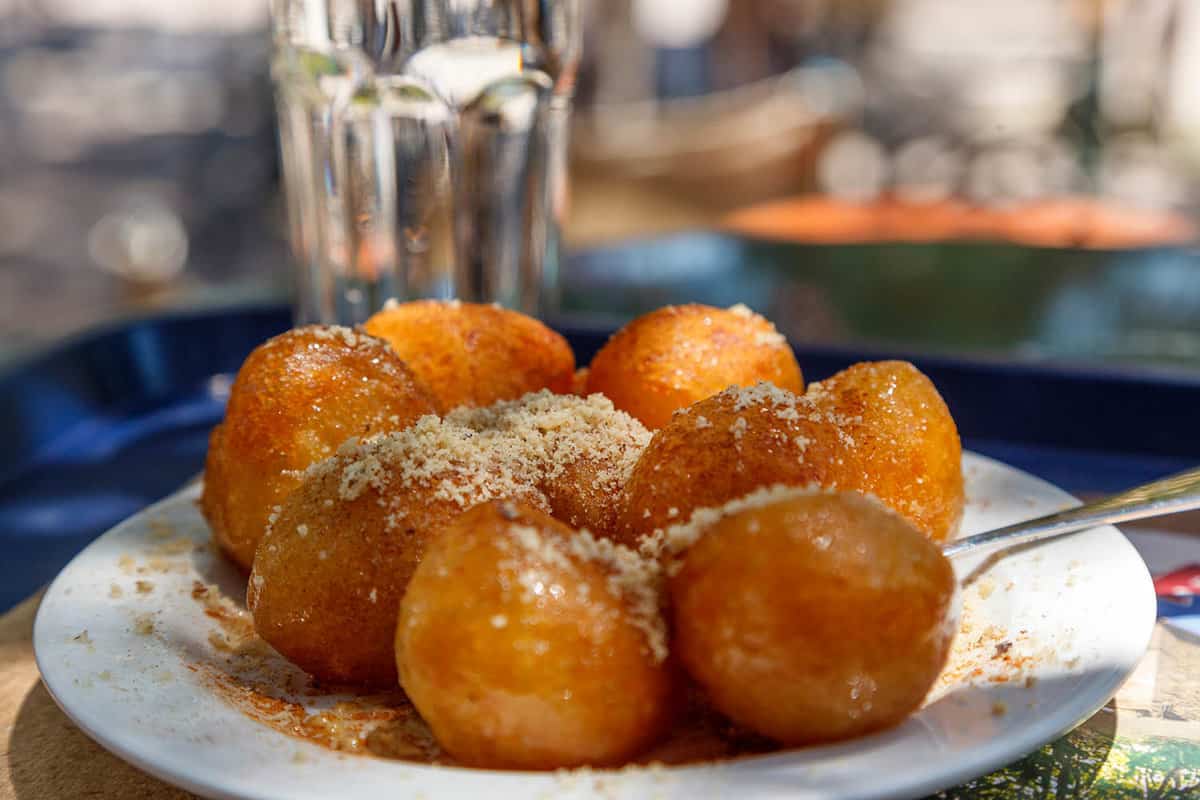 Loukoumades (Greek traditional donuts) served on a white plate along a vase of cool water