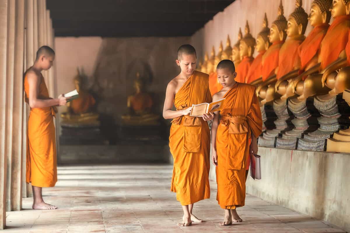 Saffron robed monks walking past statues of the Buddha