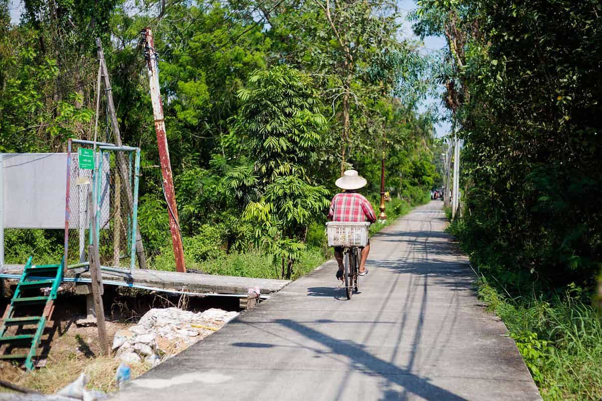 Man cycling on road wearing a Thai farmer's hat