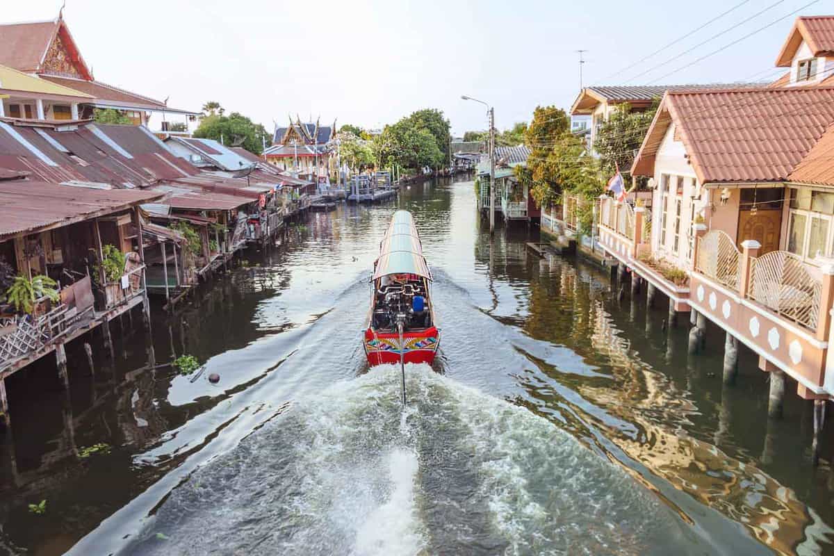 Long tail boat cruising through the canal by stilted houses