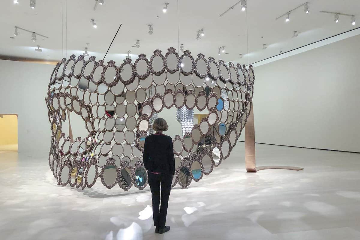 Person looking at an installation made from small mirrors, shaped like a giant mask