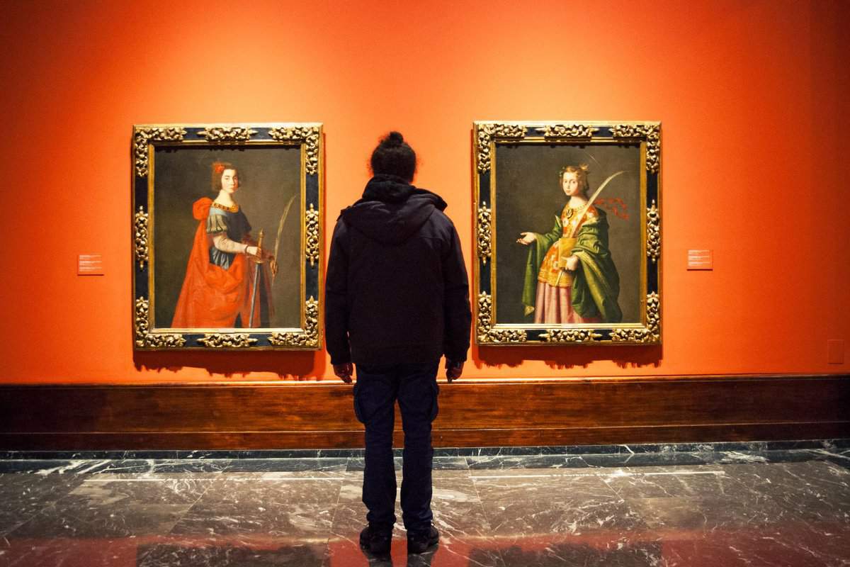 man staring at two paintings on a red wall