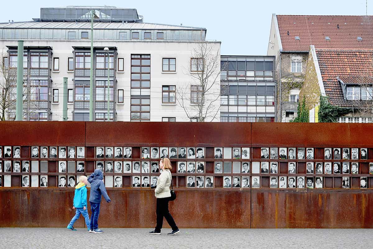 people walking past a wall covered in photos in berlin