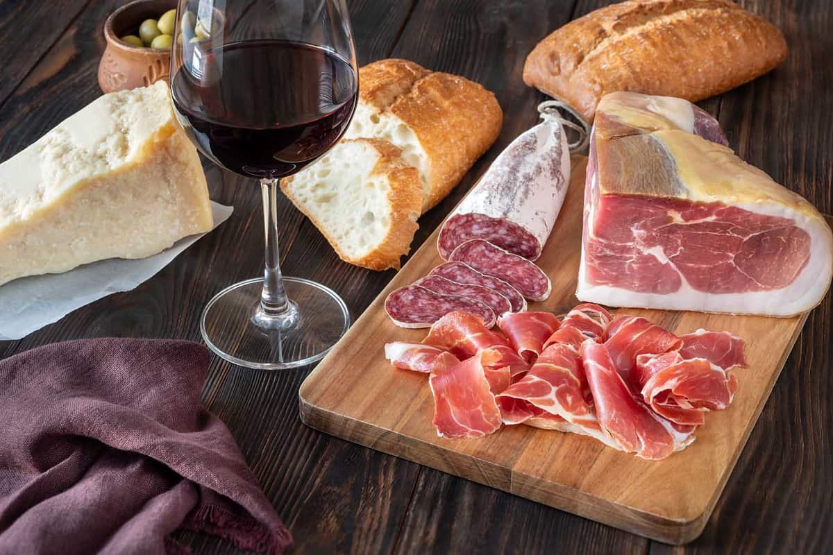 a selection of wine, bread, cheese and hams on a cutting board