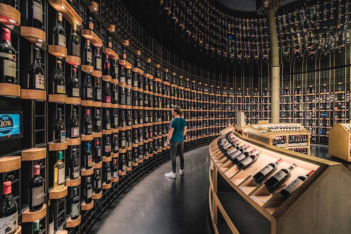 A man stands and looks at the wine in rows from floor to ceiling in a wine caviste