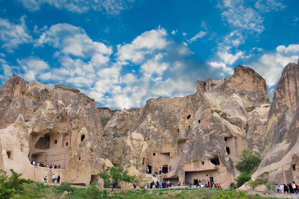 People walking into natural openings in a large rock formation.