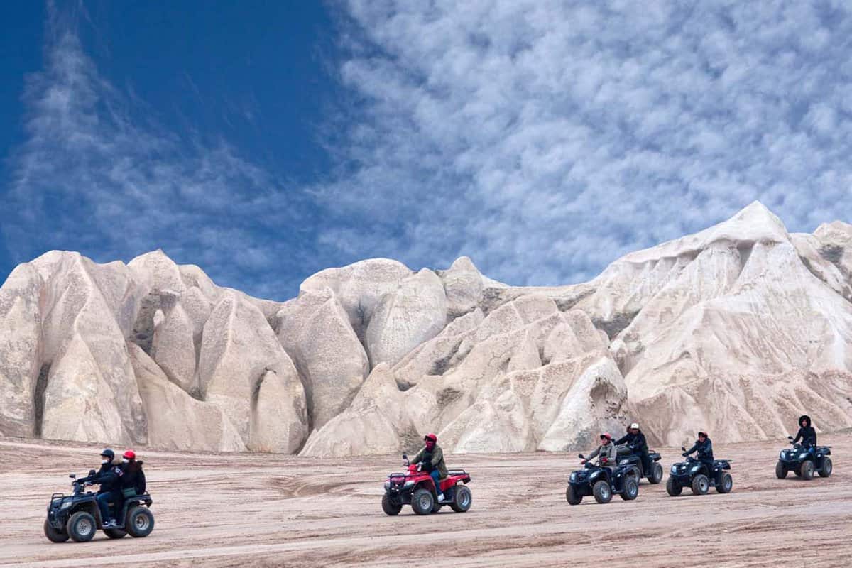 A group of people quad biking with the silhouette of white rocky mountains.