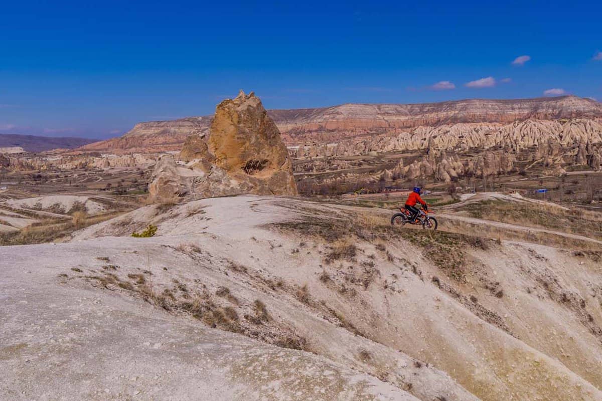 Someone biking on a mountain with the silhouette of mountains in the background.