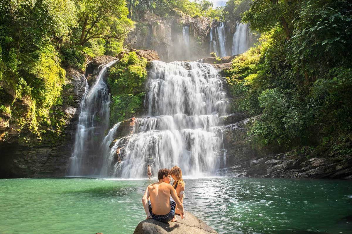a couple sat on a rock looking at waterfall