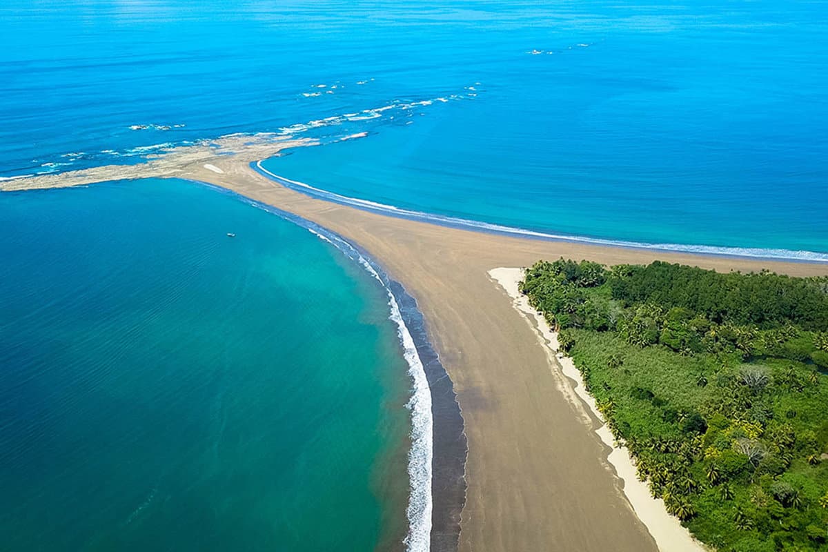 Aerial view down onto a sand spit in azure blue water