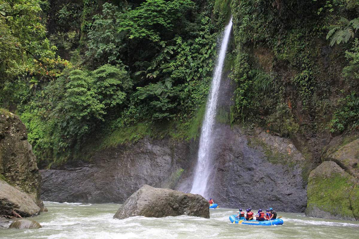 Raft approaching a high waterfall on side of the river