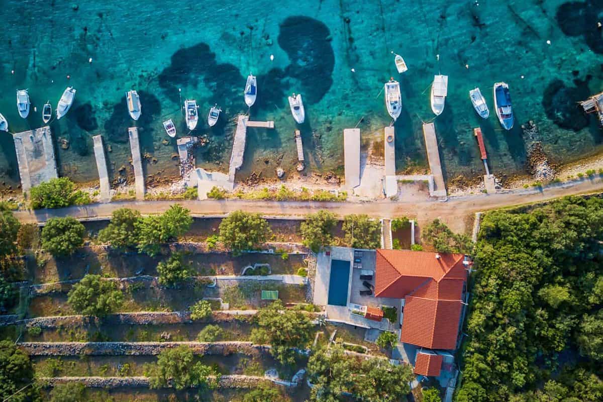 Aerial top-down view of boats moored next to a beach house by the Vela Luka lagoon