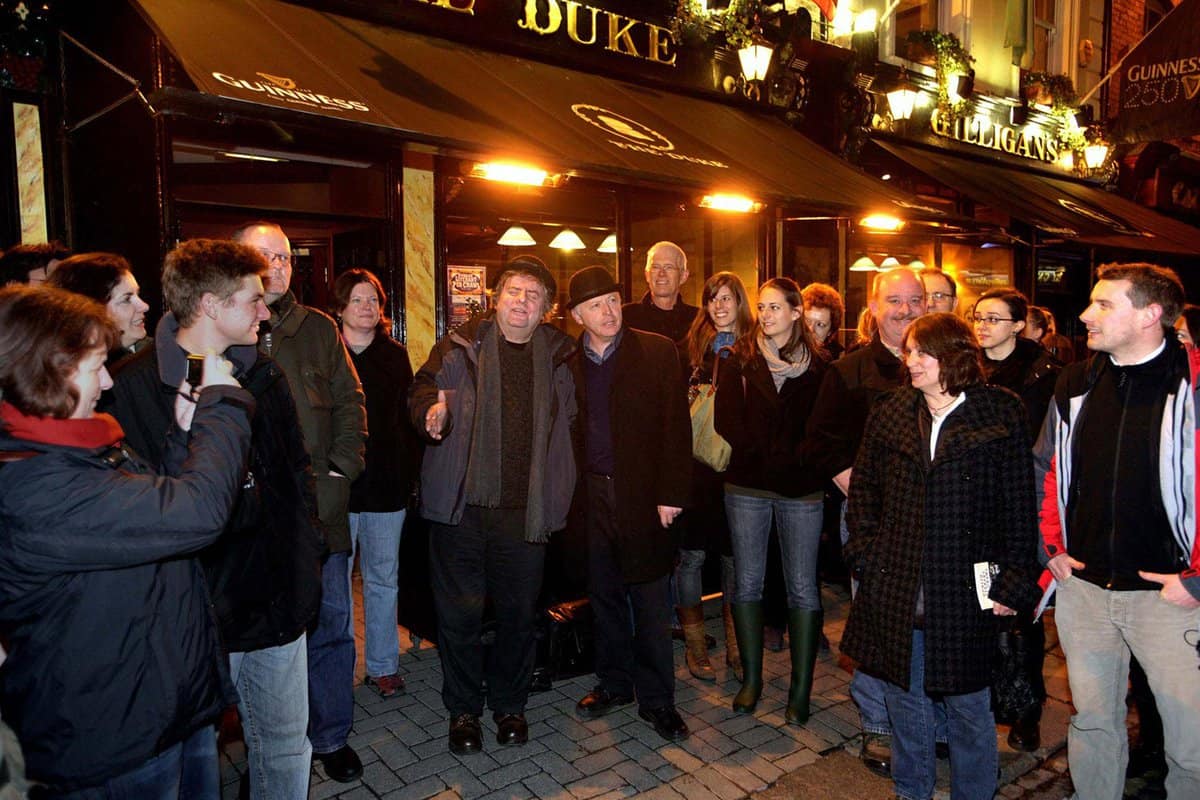 A group of tourists surrounded the two tour leaders outside of a pub