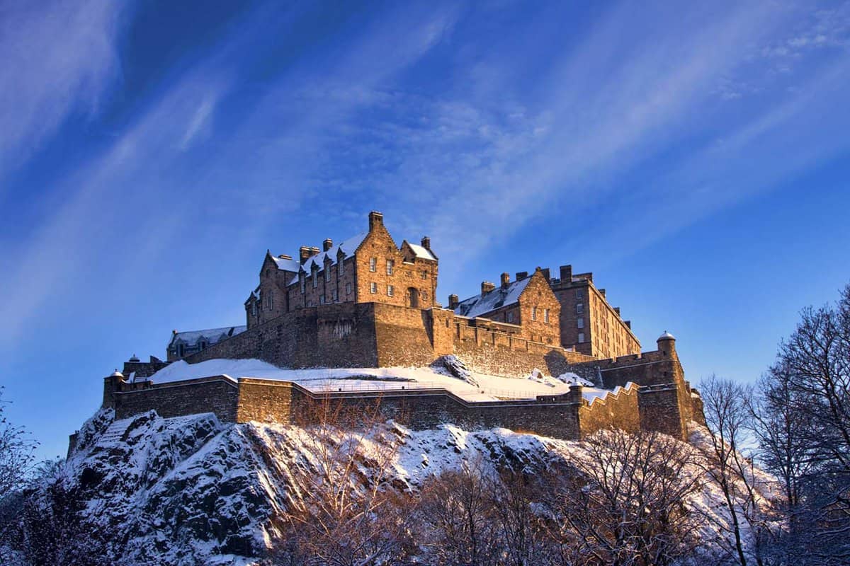 Edinburgh castle dusted with snow glows in the late afternoon blue winter sunset.