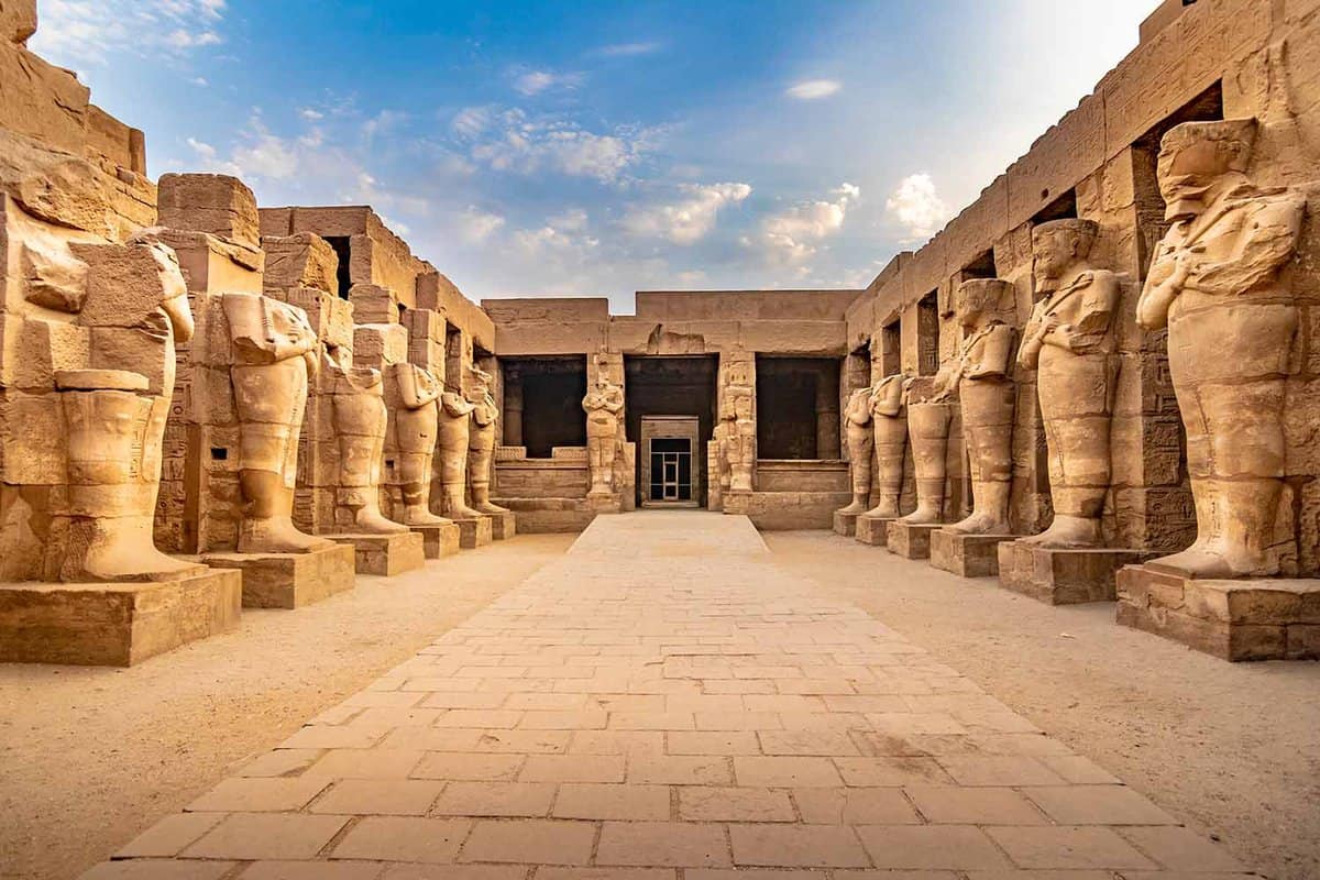 Large sculptures of pharaohs inside beautiful Egyptian landmark with hieroglyphics, and ancient symbols.