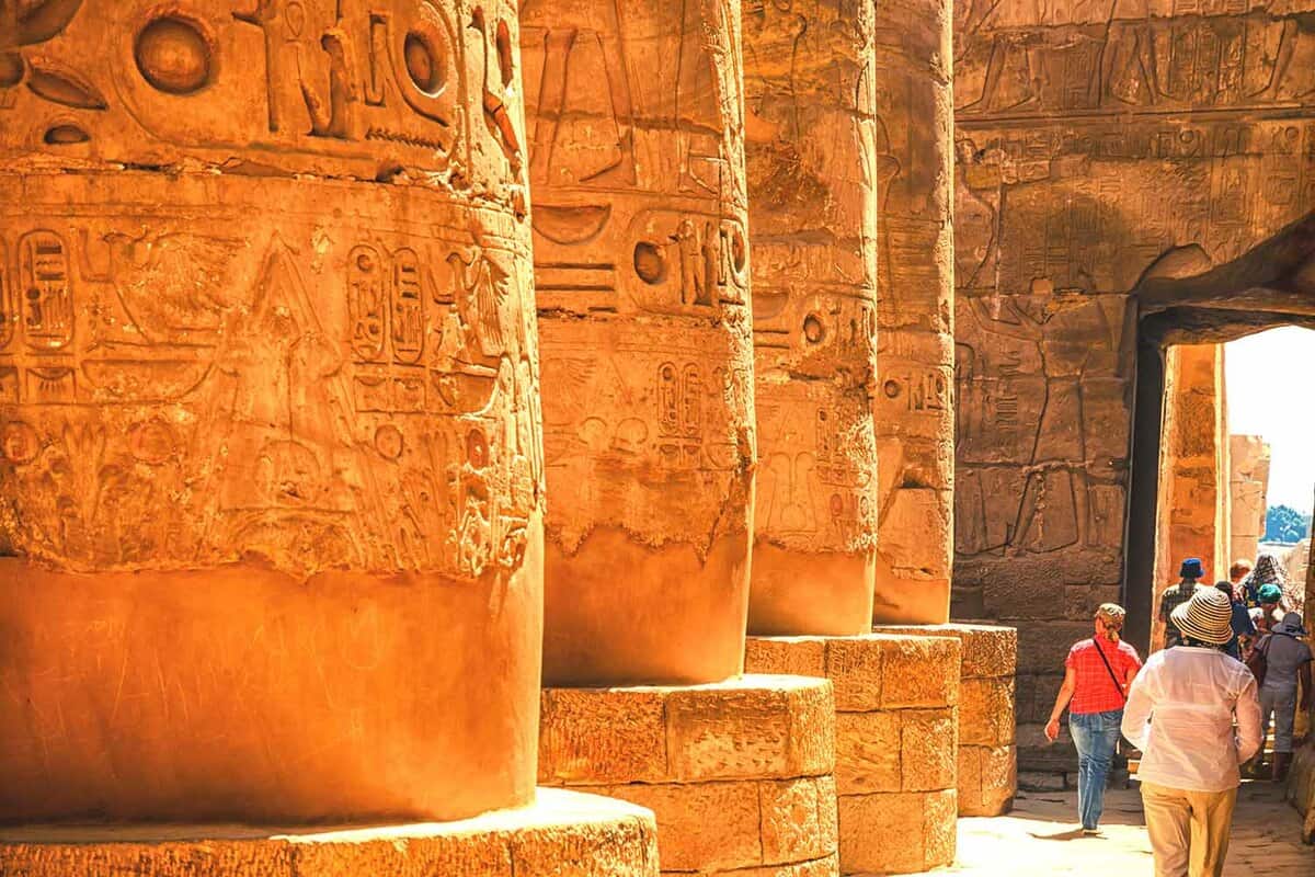 Tourists walking past The base of giant columns in the mesmerising Temple of Amun