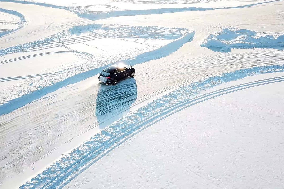 Blue car drives by icy track on snow covered lake at winter. Aerial view. Sport car racing on snow race track in winter. Driving a race car on a snowy road.