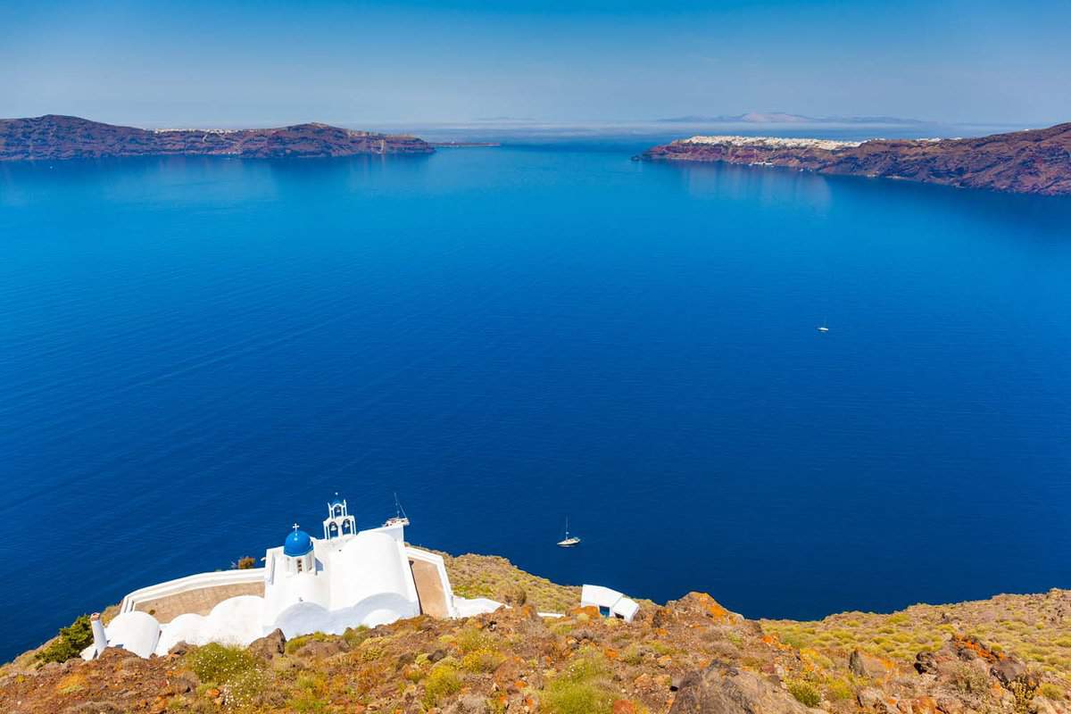 A white chapel near a cliff edge, with a bright blue sea behind it