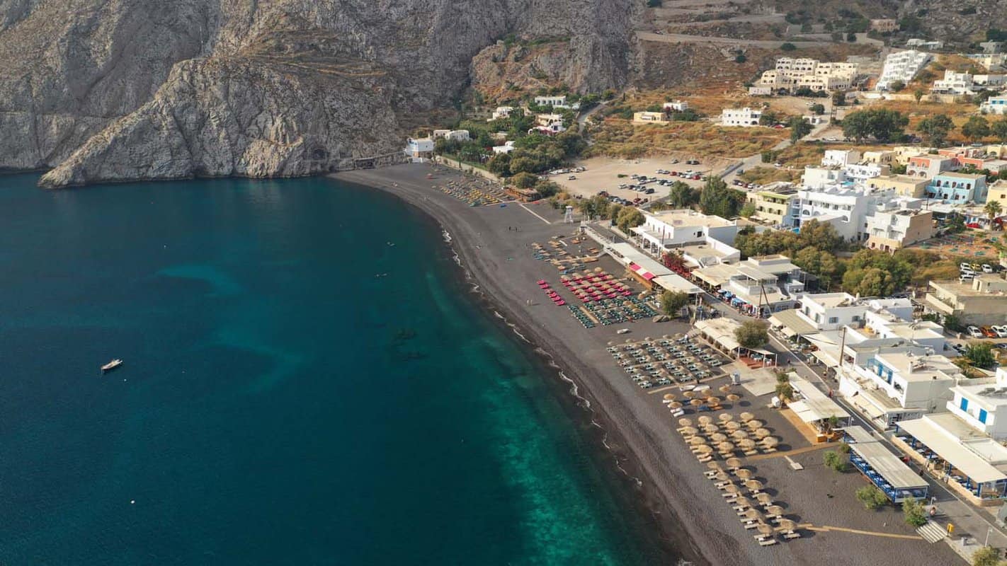 Black sand beach of Kamari seen from above, with dark blue water