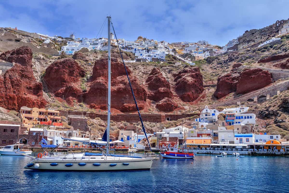Sailing yacht and boats near the harbor of Oia, Santorini island, Greece. View on red rocks caldera and white houses in the sky