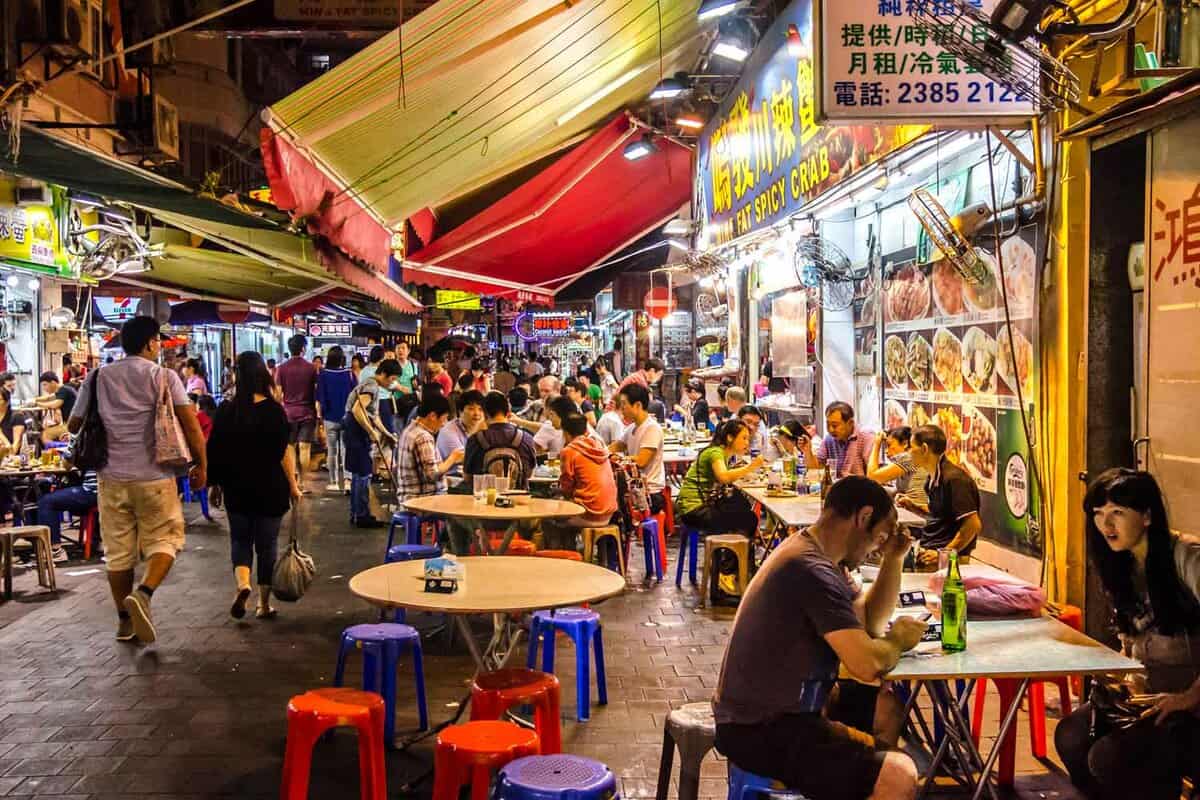 Night market on Temple Street where some people are sat eating, and others walk by
