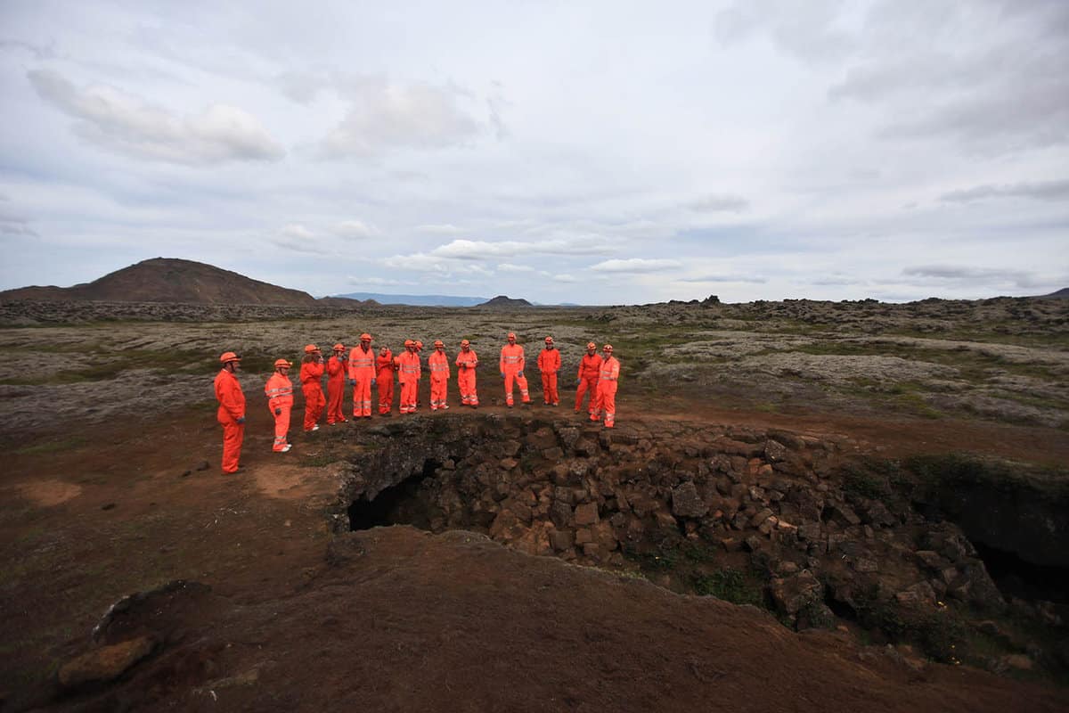A tour group in brright red suits waits at a cave mouth