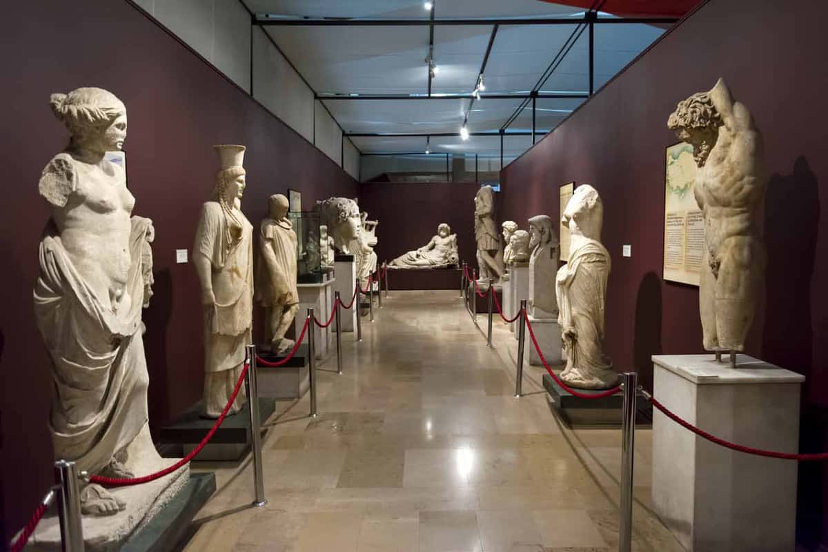View along a museum corridor with purple walls and marble statues of men and women lining each side of the passage