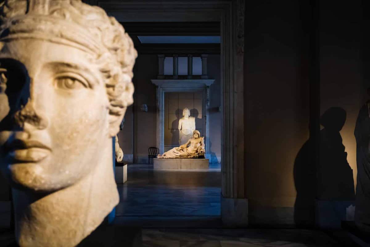 Interior of museum with marble head in the foreground and a view along a dark corridor to a well-lit statue of Oceanus reclining in the background