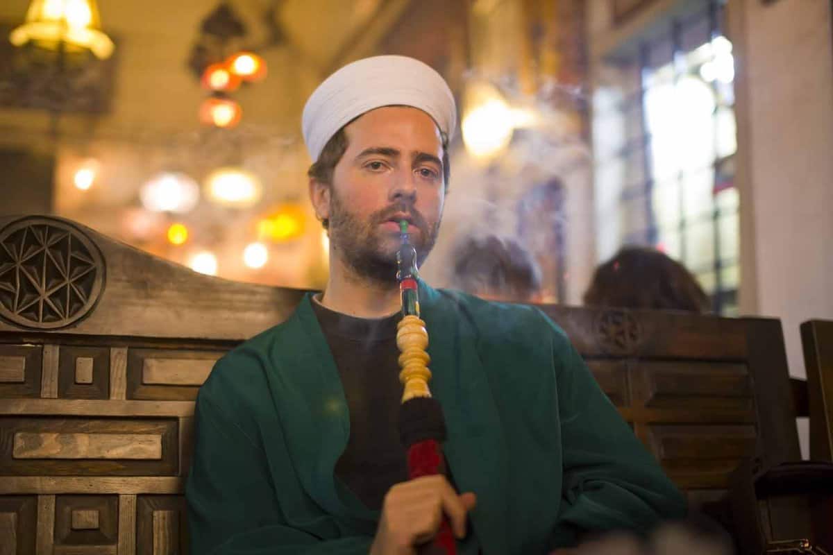 Islamic man with traditional dress smoking shisha, drinking tea