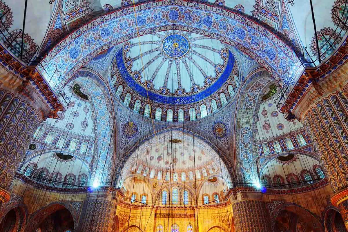 interior of a grand, domed mosque decorated with blue tiles