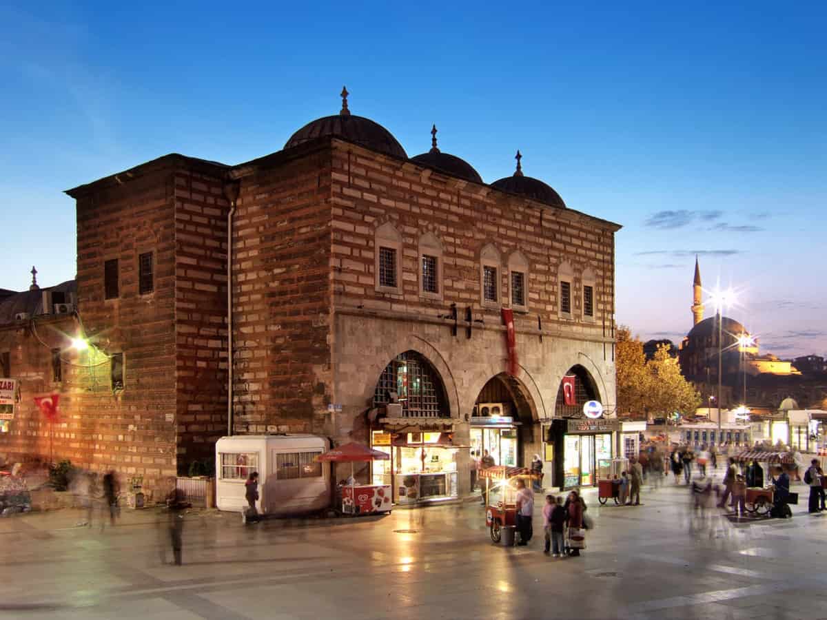 Old Turkish stone building at dusk on a marble square, serving as the entrance to a covered market