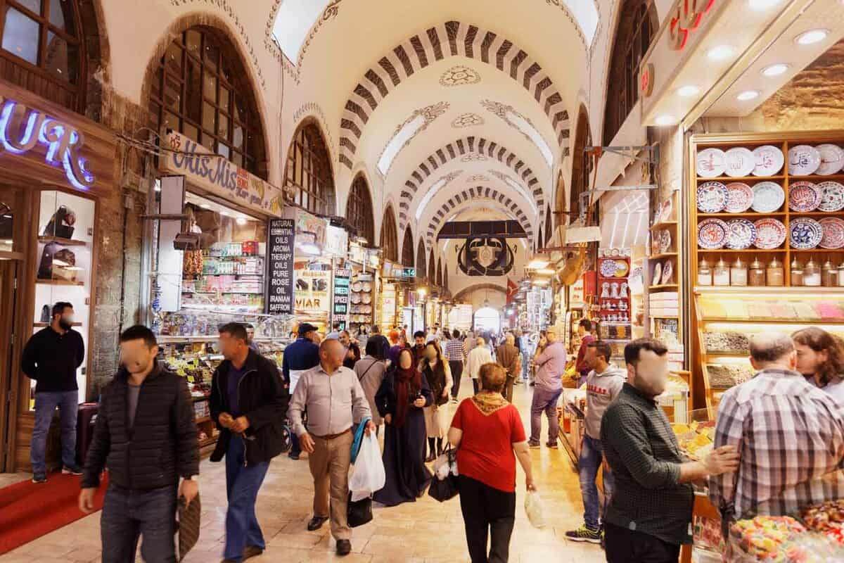 Interior of a covered market with arched ceilings and lined with small shops as tourists pass by
