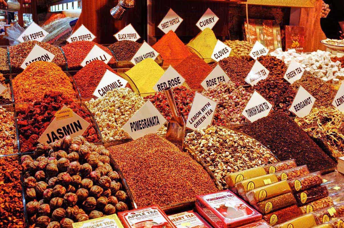 Various mounds of spices and teas in front of a shop with labels indicating what they are: jasmine, chili, red rose, peppercorn