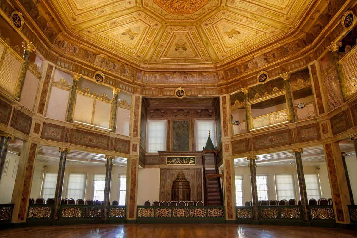 Interior of a grand, octagonal hall with a viewing gallery on the upper tier below a gilded cieling